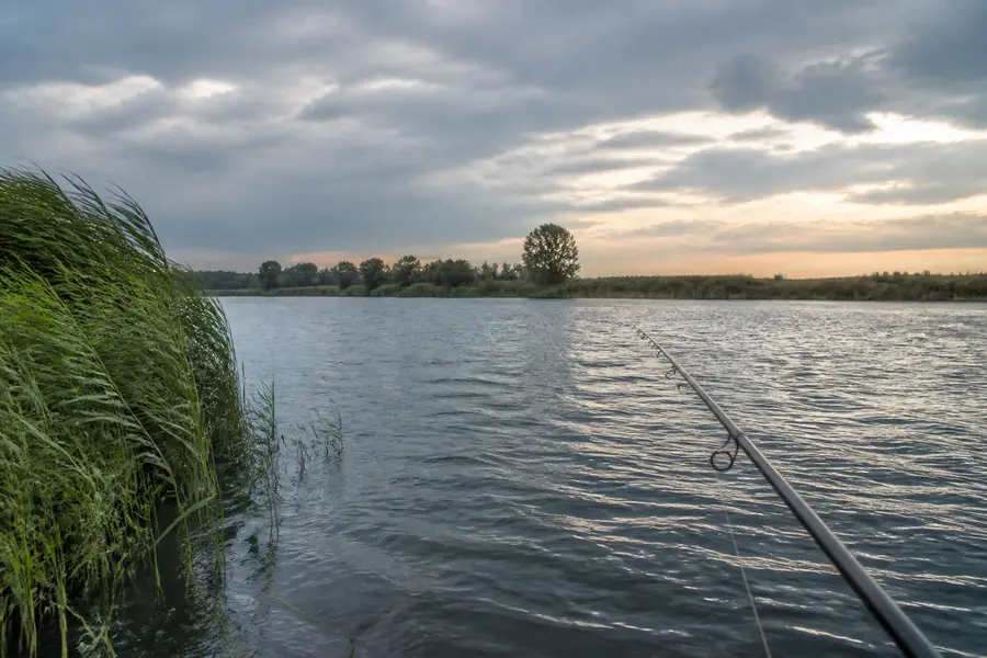 Angelrute über einem windbewegten Fluss unter wechselhaftem Himmel